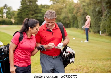 Mature Couple Playing Round Of Golf Carrying Golf Bags And Marking Scorecard - Powered by Shutterstock