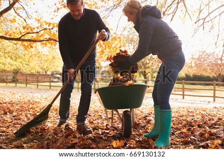 Mature Couple Raking Autumn Leaves in Garden