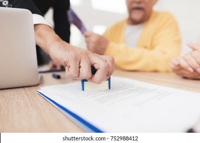 Mature couple at a reception with a lawyer. The lawyer puts a seal on the contract, the old people are happy about this. They are sitting at the desk in the lawyer's office.