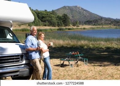 Casal maturo relaxando no campo à beira do lago em férias de motor home