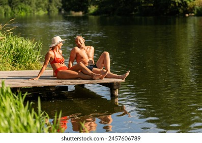 Mature couple relaxing on a dock by the lake, the woman in a hat and man smiling at each other - Powered by Shutterstock