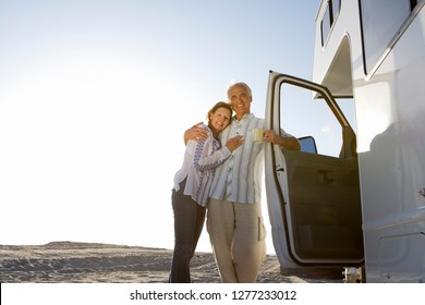 Mature Couple Relaxing On Motor Home Vacation At Beach At Camera