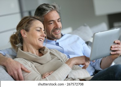 Mature couple relaxing in sofa and using digital tablet