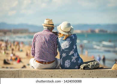 Mature Couple Of Retired Lovers Enjoying Retirement On The Beach Facing The Sea With Mobile Cell Phone Taking Pictures At Sunset. Couple Happy True Love In The Nature