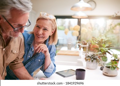 Mature Couple Reviewing And Signing Domestic Finances And Investment Paperwork In Kitchen At Home