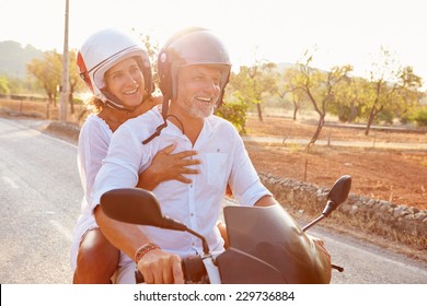 Mature Couple Riding Motor Scooter Along Country Road