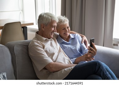 Mature Couple Sit On Sofa With Smartphone, Looking At Device Screen Take Selfie Pictures On Cellphone, Watching On-line Videos, Make Video Call Feel Happy Use Modern Wireless Tech At Home, Fun Concept