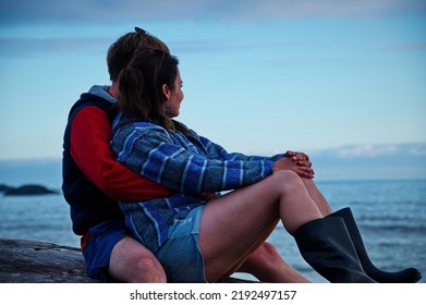 Mature Couple Sitting On A Tree Trunk On The Beach