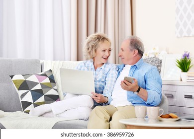 Mature Couple Sitting Together With Laptop And Mobile Phone At Home