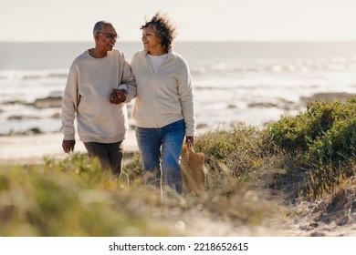 Mature couple smiling happily while walking away from the beach after a romantic picnic. Cheerful elderly couple enjoying a seaside holiday after retirement. - Powered by Shutterstock