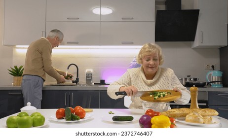 A mature couple smiling while cooking together, washing vegetables, and making a salad - Powered by Shutterstock