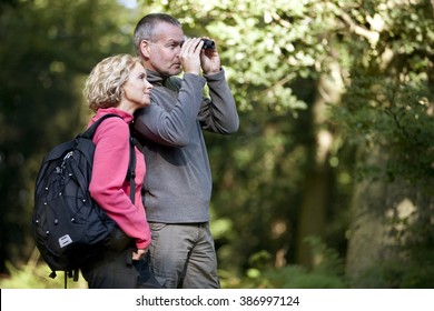 A mature couple standing in the countryside, man looking through binoculars