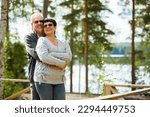Mature couple standing on porch and hugging. They are smiling and looking at the beautiful view - forest and lake. Happy senior couple embracing each other on the wooden terrace of the house. 