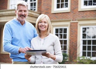 Mature Couple Standing Outside House Looking At Property Details