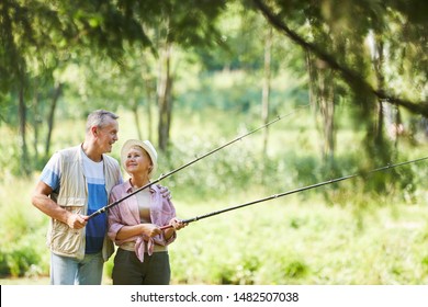 Mature Couple Standing And Talking To Each Other While Holding Fishing Rods And Fishing Together Outdoors