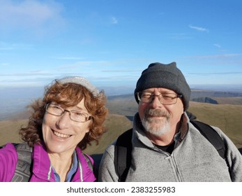 Mature couple take a selfie to share on social media while climbing Pen y Fan mountain, Brecon Beacons with a rugged landscape and sunny blue sky background. - Powered by Shutterstock