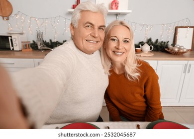 Mature couple taking selfie at table in kitchen on Christmas eve - Powered by Shutterstock