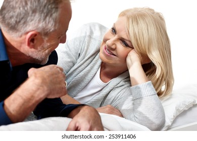 Mature Couple Talking Together On Their Bed In Bedroom 