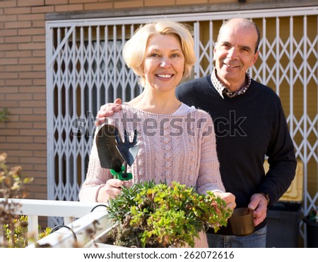 Mature couple at a terrace near their home with gardening instruments and cup of hot beverage