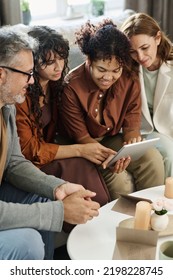 Mature Couple And Their Daughter With Her Girlfriend Gathered In Living Room For Choosing Nice Wedding Gown In Online Shop