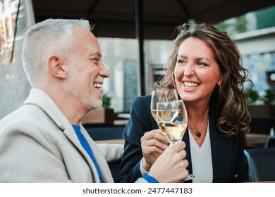 Mature couple toasting white wine glasses on a bar terrace. Middle aged married people drinking alcohol on a restaurant. Mid adult friends clinking with alcohol beverages on a date at outdoors pub - Powered by Shutterstock