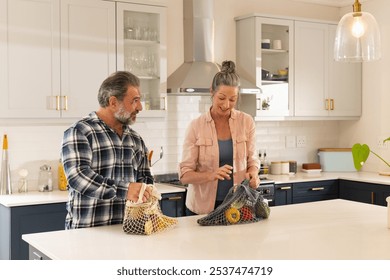 Mature couple unpacking groceries in modern kitchen, enjoying time together, at home. Food, teamwork, lifestyle, cooking, bonding - Powered by Shutterstock