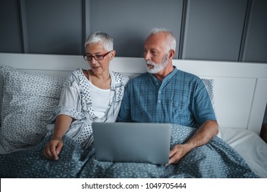 Mature couple using laptop while in bed - Powered by Shutterstock