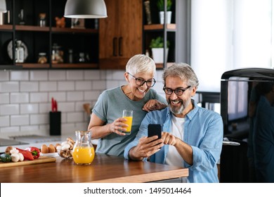 Mature Couple Using A Phone Together In The Kitchen