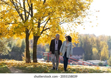 Mature Couple Walking In Autumn Park. Portrait Of A Man And Woman 50 Years Old In An Autumn Park.
