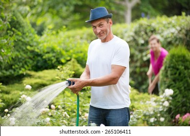 Mature Couple Watering Plants In Garden