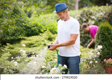 Mature Couple Watering Plants In Garden