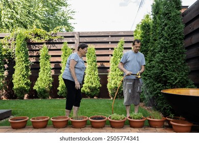 Mature couple watering plants in pots in garden on sunny day - Powered by Shutterstock