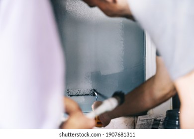 Mature Couple Working On Painting The House. Painters Paint The Wall With A Paintbrush. Paint Wall. DIY Home Decoration Renovation.