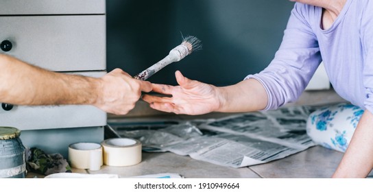 Mature Couple Working On Painting The House. Hands Of An Anonymous Wife And Husband Holding A Paintbrush. Paint Wall. DIY Home Decoration Renovation.