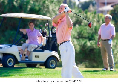 Mature couples playing golf on course with man driving ball from tee - Powered by Shutterstock