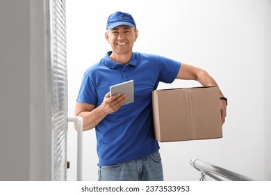 Mature courier with tablet computer and parcel in stairway