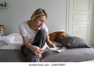 Mature Depressed Woman Widow Talks To Herself About Paying Communal Bills And Looks Disappointed. Middle-aged Female Has Absence Of Living Sense And Wants To Cry Sitting On Bed By Sleeping Dog