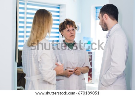 Mature doctor discussing with nurses in a hallway hospital. Doctor discussing patient case status with his medical staff after operation.