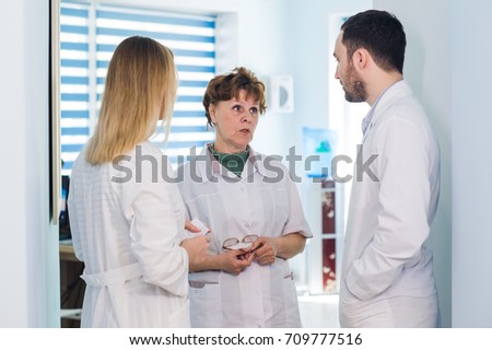 Mature doctor discussing with nurses in a hallway hospital. Doctor discussing patient case status with his medical staff after operation.