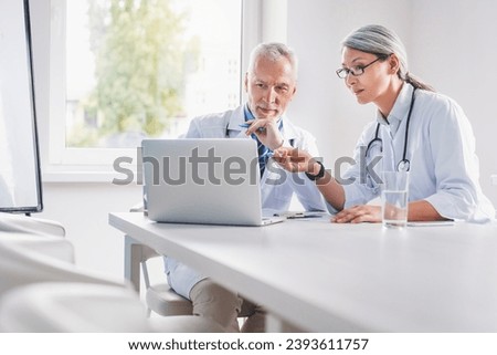 Mature doctor and his female colleague discussing together medical exam at clinic meeting room. Medical workers communicating about treatment.