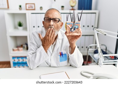 Mature Doctor Man Holding Model Of Human Anatomical Skin And Hair Covering Mouth With Hand, Shocked And Afraid For Mistake. Surprised Expression 