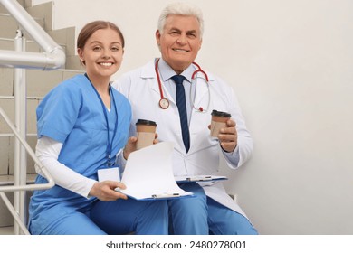 Mature doctor and nurse with coffee sitting on stairs in clinic - Powered by Shutterstock