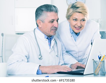 Mature Doctor And Nurse Examine Patient Data In Hospital Computer Database