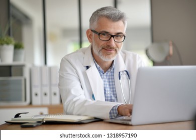 Mature Doctor In Office Working On Laptop Computer