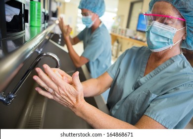 Mature doctor scrubbing hands with colleague at washbasin before surgery in hospital