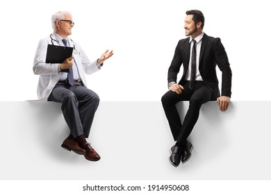 Mature Doctor Seated On A Blank Panel Gesturing And Talking To A Man In A Suit Isolated On White Background