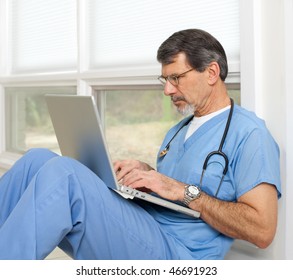 Mature Doctor Sitting On Floor Reviewing Data On His Laptop Computer. Light And Bright Exposure.