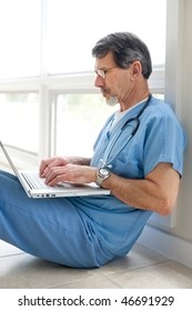 Mature Doctor Sitting On Floor Reviewing Data On His Laptop Computer. Light And Bright Exposure.