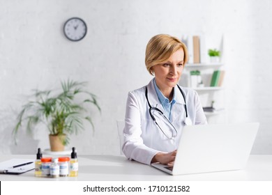 Mature Doctor Using Laptop Near Bottles With Medical Cannabis And Cbd Lettering