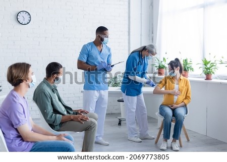 mature doctor vaccinating pregnant woman near african american colleague and patients